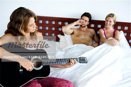 Young couple in bed listening to woman playing guitar