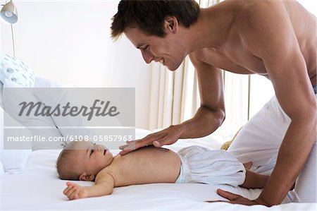 Father caressing chest's baby, lying on a bed, indoors