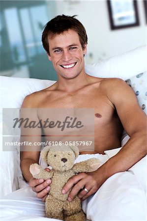 Young man smiling, looking at the camera, teddy bear in his hands, indoors