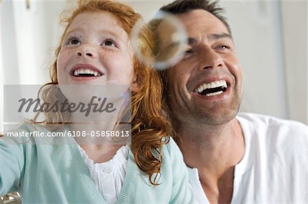 Portrait of father and daughter laughing, looking at soap bubbles, indoors