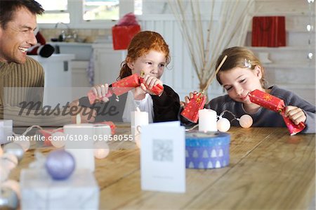 Ma  ad two children sitting around table, exchanging Christmas presents, indoors