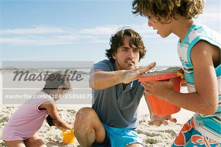 Vater und zwei Kinder spielen am Strand, im freien