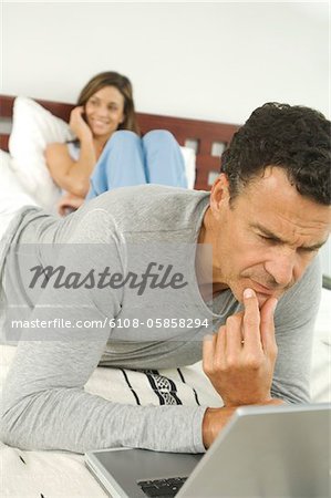 Paar im Schlafzimmer, Mann mit Laptop, drinnen
