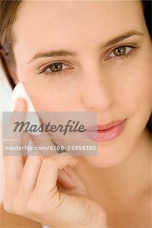 Portrait d'une femme à l'aide d'un coton de nettoyage sur sa joue, à l'intérieur