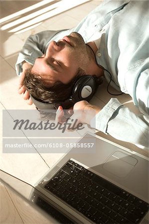 Jeune homme couché sur le plancher, écouter de la musique avec ordinateur portable