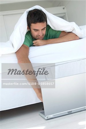 Jeune homme utilisant un ordinateur portable dans le lit