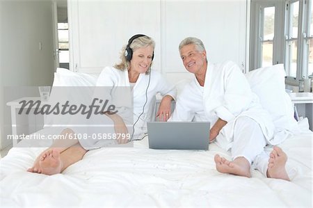 Couple in bathrobe using laptop in bed