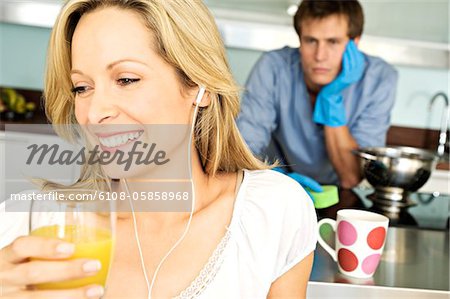 Portrait of young smiling woman holding glass of orange juice, tired man in background