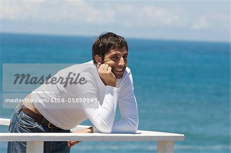 Jeune homme souriant, appuyé contre la balustrade, la mer en arrière-plan