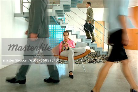 Businesswoman sitting on chair with laptop while colleagues walking on floor Businesswoman sitting on chair with laptop while colleagues walking on floor