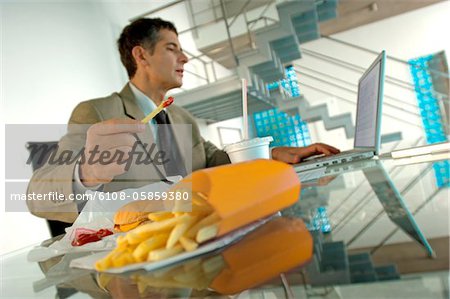 Milieu adulte homme d'affaires, manger des frites françaises, à l'aide d'ordinateur portable