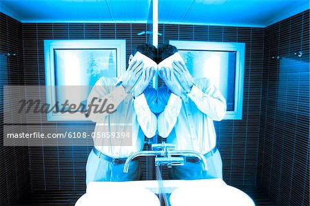 Man covering Face beim schiefen Spiegel im Waschraum