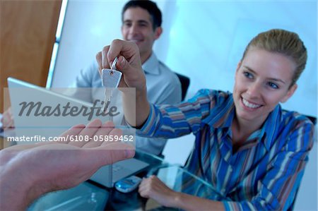 Car dealer handing key to customer, smiling