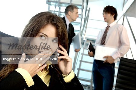 Businesswoman using mobile phone in office with colleagues in background