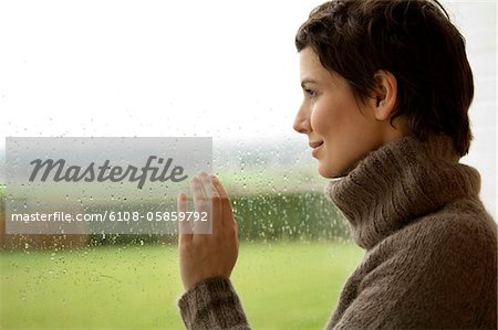 Frau mittleren Alters, Blick durch ein Fenster Frau mittleren Alters, Blick durch ein Fenster