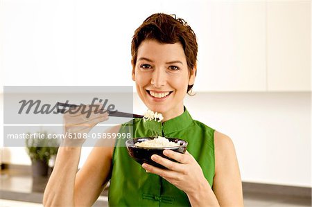 Portrait d'une femme adulte mid, manger du riz avec des baguettes