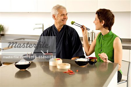 Mid adult woman feeding food to a mature man in the kitchen