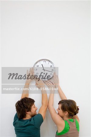 Rear view of a mid adult man and a young woman mounting a clock on the wall