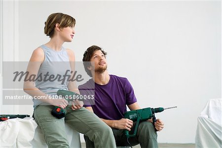Mid adult man and a young woman sitting in a room and holding drills