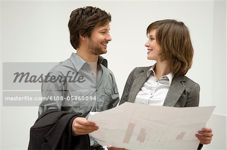 Mid adult man and a young woman holding a blueprint and looking at each other