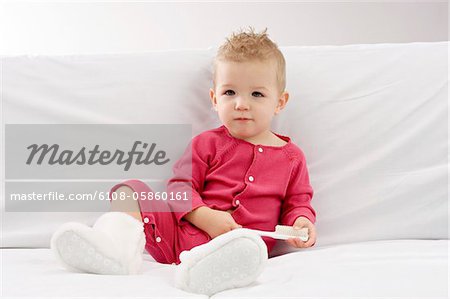 Portrait of a baby boy sitting on a couch and holding a brush