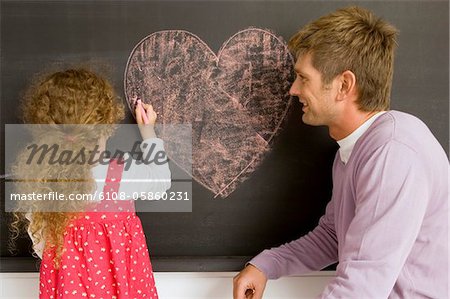 Fille de dessin sur un tableau noir avec son père la regarder