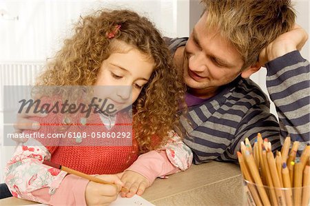 Girl drawing with her father sitting beside her