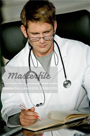 Close-up of a male doctor sitting at a desk and reading a notebook
