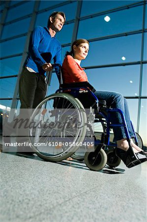 Profil de côté d'un homme adult milieu pousser une jeune femme assise dans un fauteuil roulant