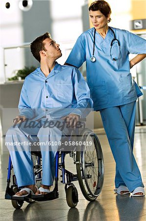 Male patient sitting in a wheelchair and looking at a female doctor standing beside him