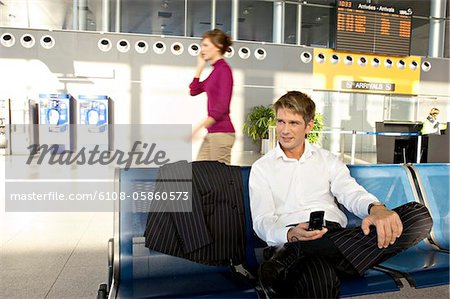 Businessman holding a mobile phone and sitting at an airport lounge