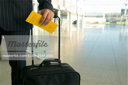 Mid section view of a businessman holding a luggage and an airplane ticket