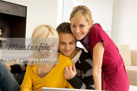 Two young women with a young man in front of a laptop