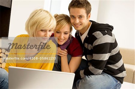 Two young women and a young man sitting in front of a laptop and smiling