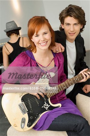 Portrait of a young woman playing a guitar with a teenage boy sitting beside her