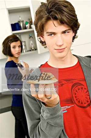 Close-up of a teenage boy holding a slice of pizza and a young woman standing behind him