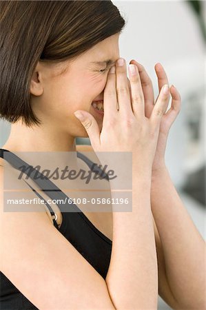 Side profile of a young woman laughing and covering mouth with hands