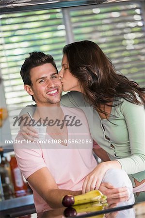 Woman holding a cup of yogurt and kissing a man