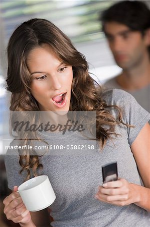 Woman text messaging on a mobile phone and looking surprised