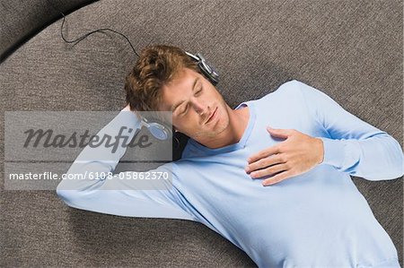 Mann auf einem runden Sofa liegend und Musik hören