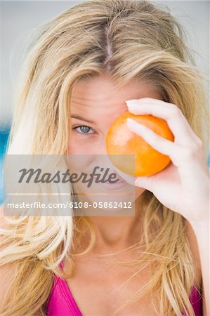 Close-up of a woman holding an orange in front of her eye