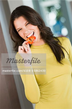 Woman eating a slice of red bell pepper