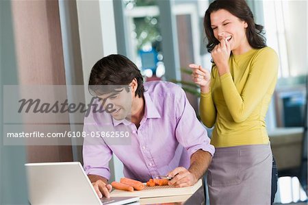 Cuisiner avec la recette sur un ordinateur portable et d'une femme riant de lui l'homme