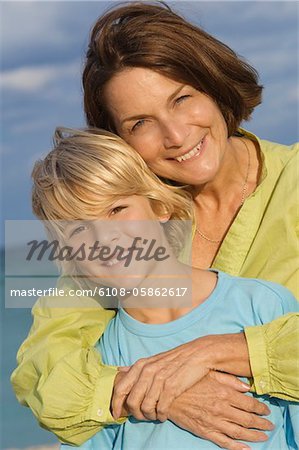 Frau umarmt ihren Enkel von hinten am Strand