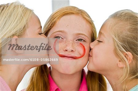 Close-up of two girls kissing their friend