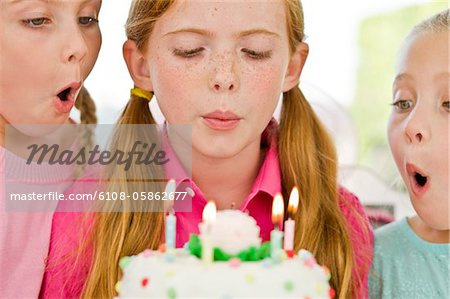Close-up of three girls blowing out candles on a birthday cake