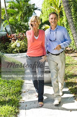 Man pulling his luggage beside a woman talking on a mobile phone