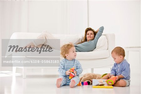 Babies playing with toys and their mother resting on a couch