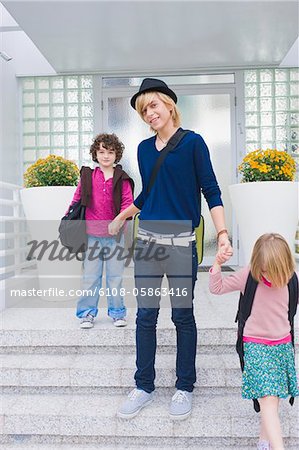 Teenage boy holding hands of schoolchildren