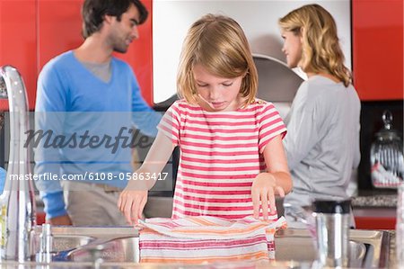 Girl holding dish cloth with her parents standing in the background